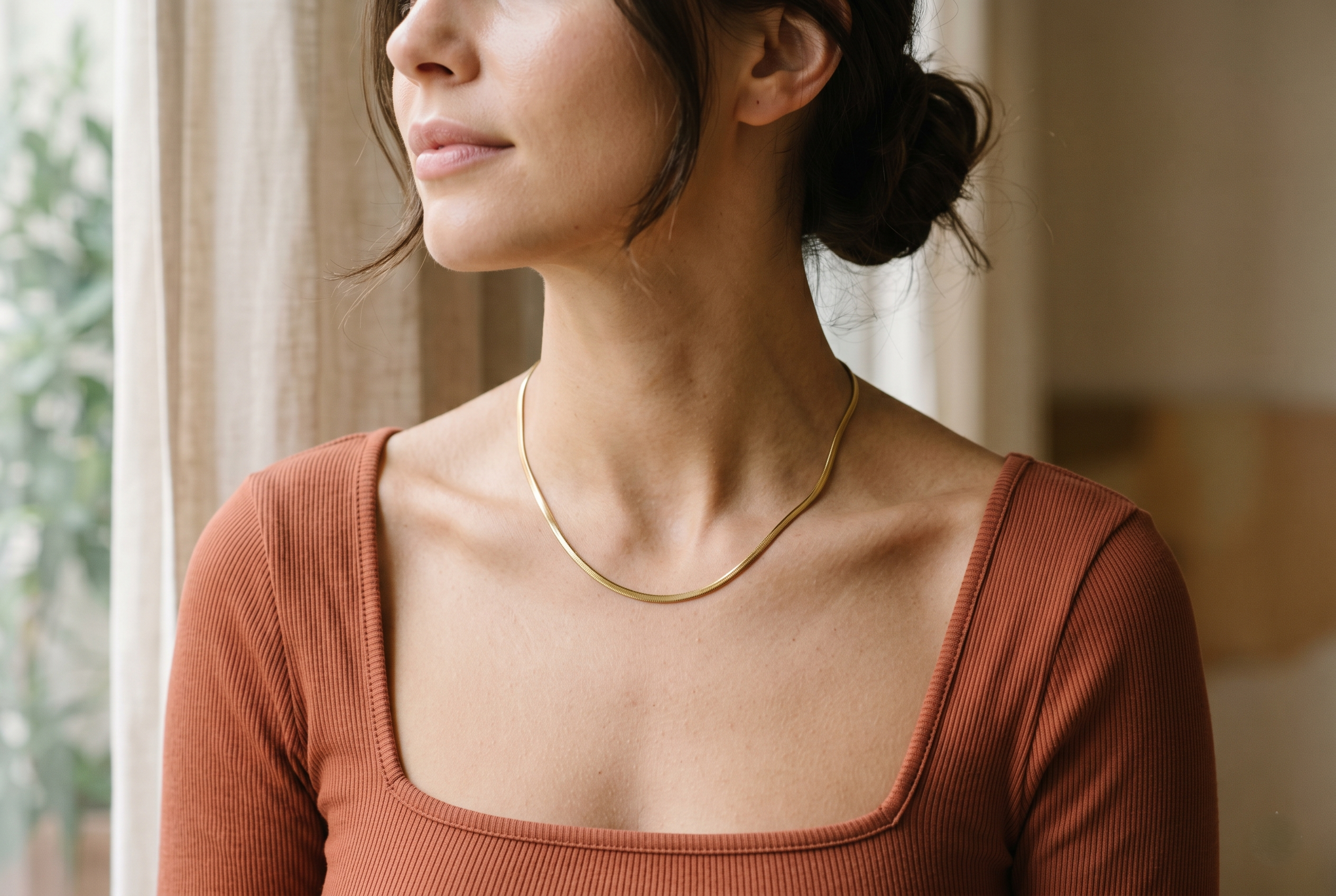 Close-up of a woman's neckline wearing a minimalist snake chain necklace in gold stainless steel, square neck bodysuit, soft natural light, elegant and clean aesthetic